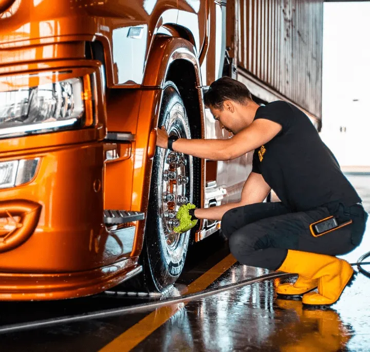 Truckwash medewerker in werkkleding poetst een oranje truck